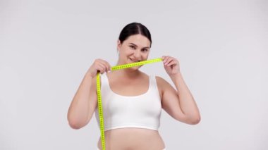 Kilolu bir kadın beyaz arka planda mezurayla poz veriyor.