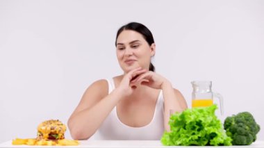 Hamburger ve sağlıklı yiyecek arasında seçim yapan genç bir kadın model.