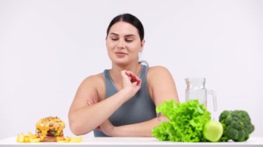 Hamburger ve sağlıklı yiyecek arasında seçim yapan genç bir kadın model.