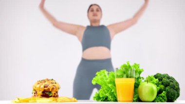 Fast food masada sağlıklı yiyeceğe karşı, arka planda egzersiz yapan genç kadın.