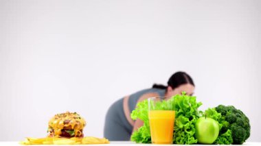 Fast food masada sağlıklı yiyeceğe karşı, arka planda egzersiz yapan genç kadın.
