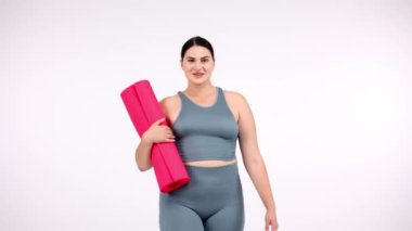 Beyaz arka planda pembe yoga minderi olan güzel bir genç kadın.