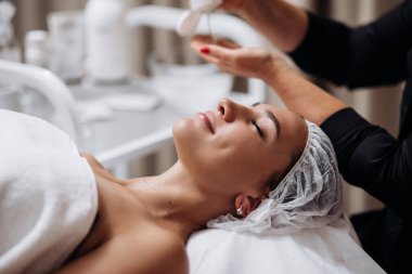 Kozmetik uzmanı güzellik salonunda yüz ve boyun masajı yapıyor. Kişisel bakım spa konsepti. Çekici ve rahatlatıcı bir kadının portresi. Kozmetik bilimi ve temizlik reklamları.