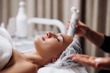 Kozmetik uzmanı güzellik salonunda yüz ve boyun masajı yapıyor. Kişisel bakım spa konsepti. Çekici ve rahatlatıcı bir kadının portresi. Kozmetik bilimi ve temizlik reklamları.