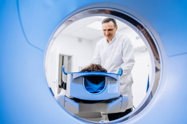 Genç adam tomografiye giriyor. Bilgisayarlı tomografi tarayıcısındaki erkek hastayı gözden kaçıran CT tarama teknolojisi uzmanı prosedür hazırlığı sırasında