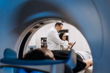 İki doktor teşhisi tartışırken, MRI makinesindeki genç adam modern hastanedeki tıbbi muayenede