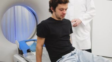 Genç adam tomografiye giriyor. Bilgisayarlı tomografi tarayıcısındaki erkek hastayı gözden kaçıran CT tarama teknolojisi uzmanı prosedür hazırlığı sırasında