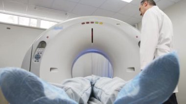 Genç adam tomografiye giriyor. Bilgisayarlı tomografi tarayıcısındaki erkek hastayı gözden kaçıran CT tarama teknolojisi uzmanı prosedür hazırlığı sırasında