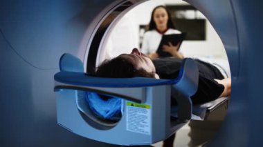 MR makinesinde genç bir adam. Bu arada iki doktor modern hastanede arka plan üzerinde çalışıyor.