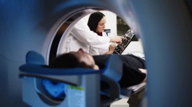 İki doktor teşhisi tartışırken, MRI makinesindeki genç adam modern hastanedeki tıbbi muayenede