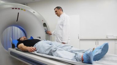 Genç adam tomografiye giriyor. Bilgisayarlı tomografi tarayıcısındaki erkek hastayı gözden kaçıran CT tarama teknolojisi uzmanı prosedür hazırlığı sırasında
