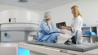 Beyaz cüppeli kadın doktor hastayla MRI taramasına bakıyor.