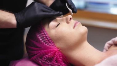 Bir kozmetik uzmanının kaplıca salonundaki müşterisinin yüzüne maske taktığı yakın plan fotoğraf. Bu sahne, huzurlu ve profesyonel bir ortamda cilt bakımının özenli uygulamasını vurgular..