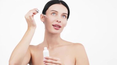 Güzel esmer kadının portresi beyaz arka planda serum uyguluyor.           