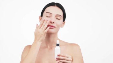 Güzel esmer kadının portresi beyaz arka planda serum uyguluyor.           
