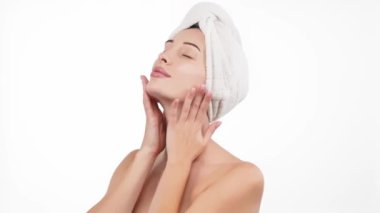 Kafasında havluyla güzel bir kadın beyaz arka planda kusursuz tenine hafifçe dokunuyor.        