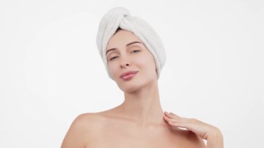 Kafasında havluyla güzel bir kadın beyaz arka planda kusursuz tenine hafifçe dokunuyor.        