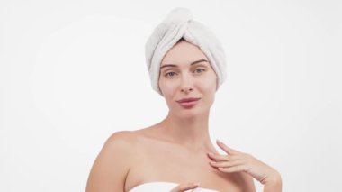 Kafasında havluyla güzel bir kadın beyaz arka planda kusursuz tenine hafifçe dokunuyor.        