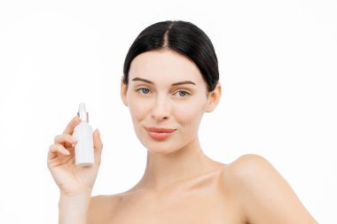 Güzel bir esmer kadının portresi kozmetik ürünlerle dolu bir şişe tutuyor ve beyaz arka planda izole edilmiş kameraya bakıyor.             