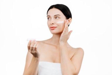Güzel esmer kadının portresi beyaz arka planda izole edilmiş nemlendirici krem sürüyor.      