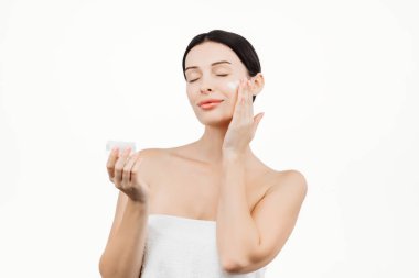 Güzel esmer kadının portresi beyaz arka planda izole edilmiş nemlendirici krem sürüyor.      