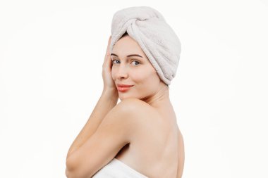 Kafasında havluyla beyaz arka planda kameraya gülümseyen güzel bir genç kadının portresi.