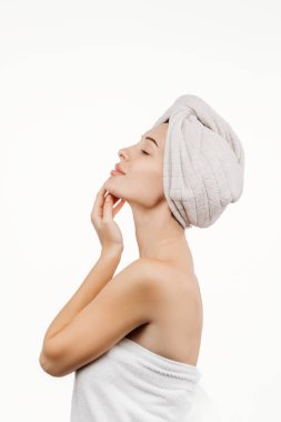 Kafasında havluyla tenine dokunan güzel genç bir kadın beyaz arka planda izole edilmiş.    