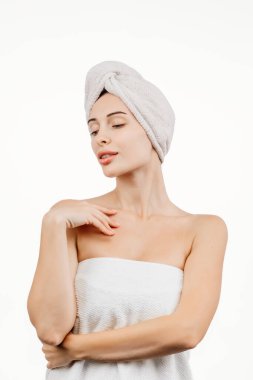 Kafasında havluyla tenine dokunan güzel genç bir kadın beyaz arka planda izole edilmiş.    