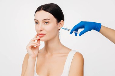 Genç ve güzel bir kadın beyaz bir stüdyo geçmişine karşı botoks yaptırıyor..