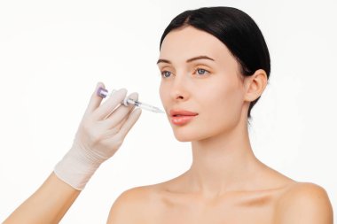 Doktor eli, kadın yüzüne yakın bir şırınga tutuyor ve cilt kaldırma iğnesi oluyor. Bu anda güzellik ve modern cilt teknikleri ışıltılı bir görünüm için vurgulanıyor..