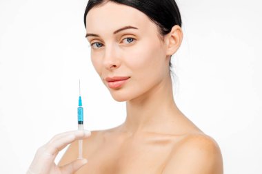 Doktor eli, kadın yüzüne yakın bir şırınga tutuyor ve cilt kaldırma iğnesi oluyor. Bu anda güzellik ve modern cilt teknikleri ışıltılı bir görünüm için vurgulanıyor..