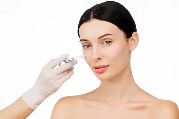 Doktor eli, kadın yüzüne yakın bir şırınga tutuyor ve cilt kaldırma iğnesi oluyor. Bu anda güzellik ve modern cilt teknikleri ışıltılı bir görünüm için vurgulanıyor..