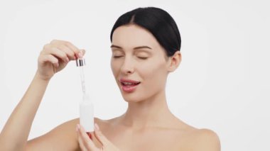 Güzel esmer kadının portresi beyaz arka planda serum uyguluyor.           