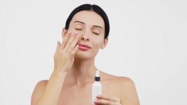Güzel esmer kadının portresi beyaz arka planda serum uyguluyor.           