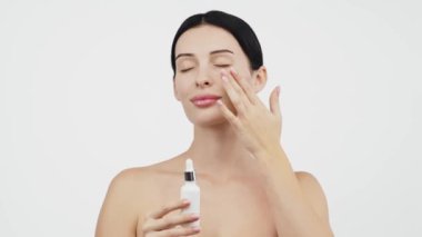 Güzel esmer kadının portresi beyaz arka planda serum uyguluyor.           