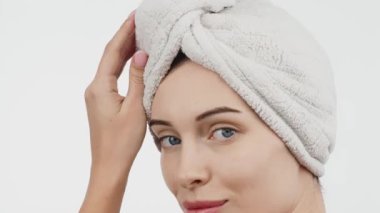 Kafasında havluyla güzel bir kadın beyaz arka planda kusursuz tenine hafifçe dokunuyor.        