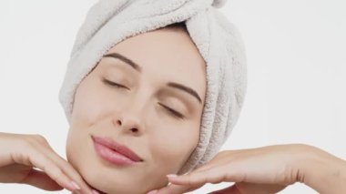 Kafasında havluyla güzel bir kadın beyaz arka planda kusursuz tenine hafifçe dokunuyor.        