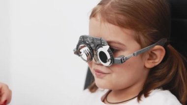 Gözlük takan küçük bir kız göz doktorunun ofisinde görüş kontrolünden geçiyor. Çocukların vizyonlarını tanımlamak ve tedavi etmek için modern yöntemlere bir örnek.