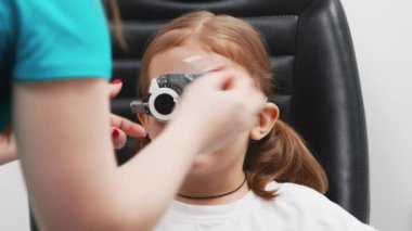 Gözlük takan küçük bir kız göz doktorunun ofisinde görüş kontrolünden geçiyor. Çocukların vizyonlarını tanımlamak ve tedavi etmek için modern yöntemlere bir örnek.
