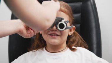 Gözlük takan küçük bir kız göz doktorunun ofisinde görüş kontrolünden geçiyor. Çocukların vizyonlarını tanımlamak ve tedavi etmek için modern yöntemlere bir örnek.