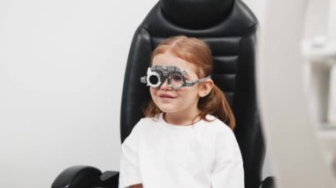 Gözlük takan küçük bir kız göz doktorunun ofisinde görüş kontrolünden geçiyor. Çocukların vizyonlarını tanımlamak ve tedavi etmek için modern yöntemlere bir örnek.