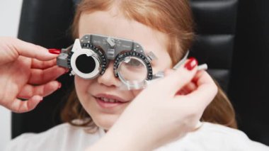 Gözlük takan küçük bir kız göz doktorunun ofisinde görüş kontrolünden geçiyor. Çocukların vizyonlarını tanımlamak ve tedavi etmek için modern yöntemlere bir örnek.