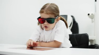Gözlük takan küçük bir kız göz doktorunun ofisinde görüş kontrolünden geçiyor. Çocukların vizyonlarını tanımlamak ve tedavi etmek için modern yöntemlere bir örnek.