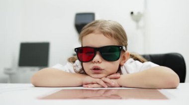 Gözlük takan küçük bir kız göz doktorunun ofisinde görüş kontrolünden geçiyor. Çocukların vizyonlarını tanımlamak ve tedavi etmek için modern yöntemlere bir örnek.