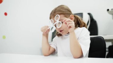 Gözlük takan küçük bir kız göz doktorunun ofisinde görüş kontrolünden geçiyor. Çocukların vizyonlarını tanımlamak ve tedavi etmek için modern yöntemlere bir örnek.