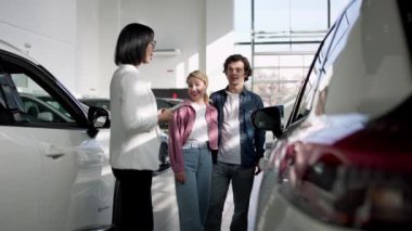 Galeride müşterilere yardım etmek için dijital tablet kullanan bir kadın araba satıcısı. Kendine güvenen araba satıcısı, alıcılarla yeni bir arabanın indirimlerini ve faydalarını tartışıyor.