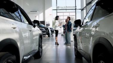 Galeride müşterilere yardım etmek için dijital tablet kullanan bir kadın araba satıcısı. Kendine güvenen araba satıcısı, alıcılarla yeni bir arabanın indirimlerini ve faydalarını tartışıyor.