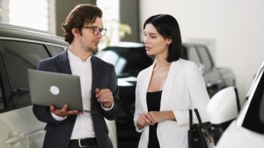 Kendine güvenen araba satıcısı, alıcıyla yeni bir arabanın indirimlerini ve faydalarını tartışıyor.. 
