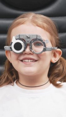 Gözlük takan küçük bir kız göz doktorunun ofisinde görüş kontrolünden geçiyor. Çocukların vizyonlarını tanımlamak ve tedavi etmek için modern yöntemlere bir örnek.