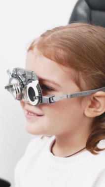 Gözlük takan küçük bir kız göz doktorunun ofisinde görüş kontrolünden geçiyor. Çocukların vizyonlarını tanımlamak ve tedavi etmek için modern yöntemlere bir örnek.